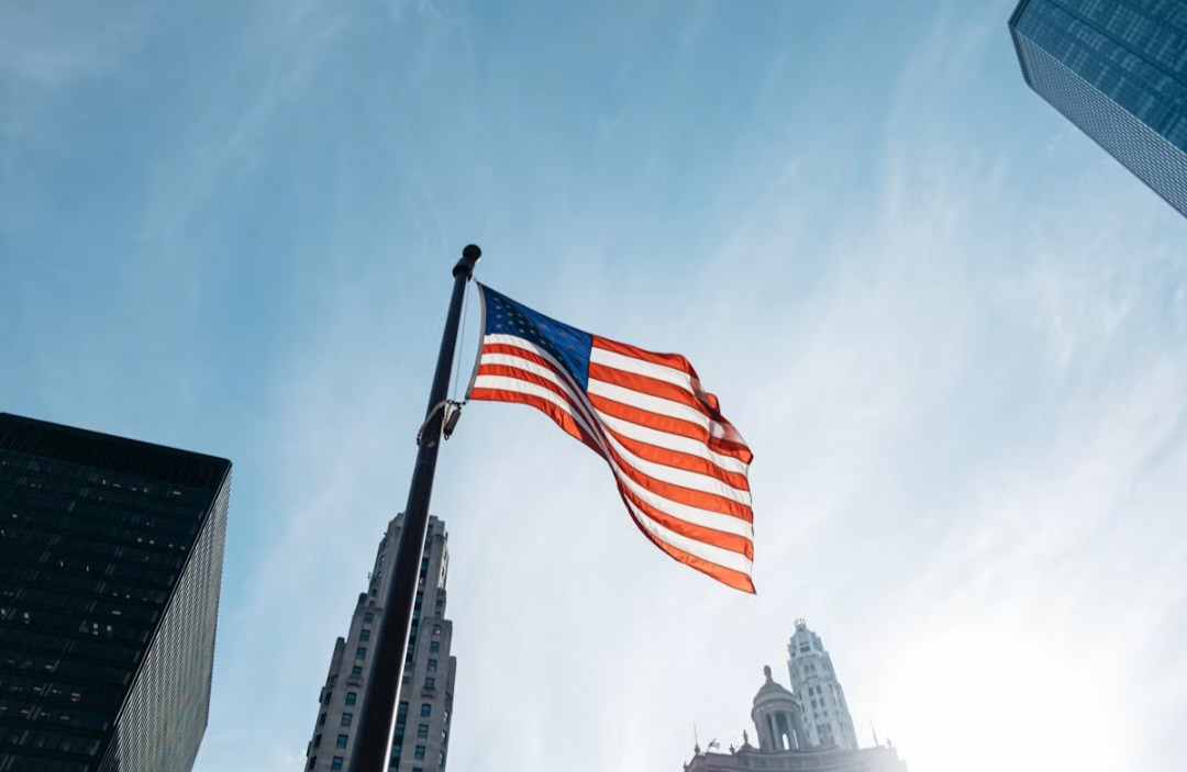 A United States flag flying between skyscrapers against a bright blue sky